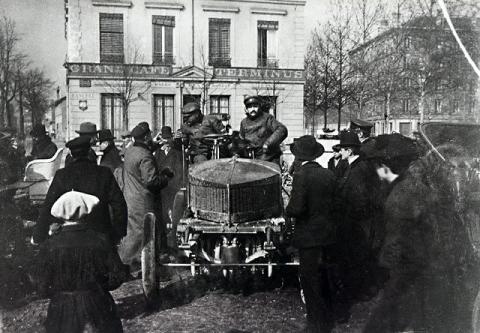 Early automobile surrounded by spectators